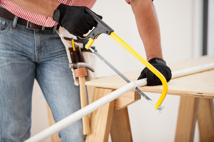 Closeup of a plumber using a hacksaw to cut down some pipes